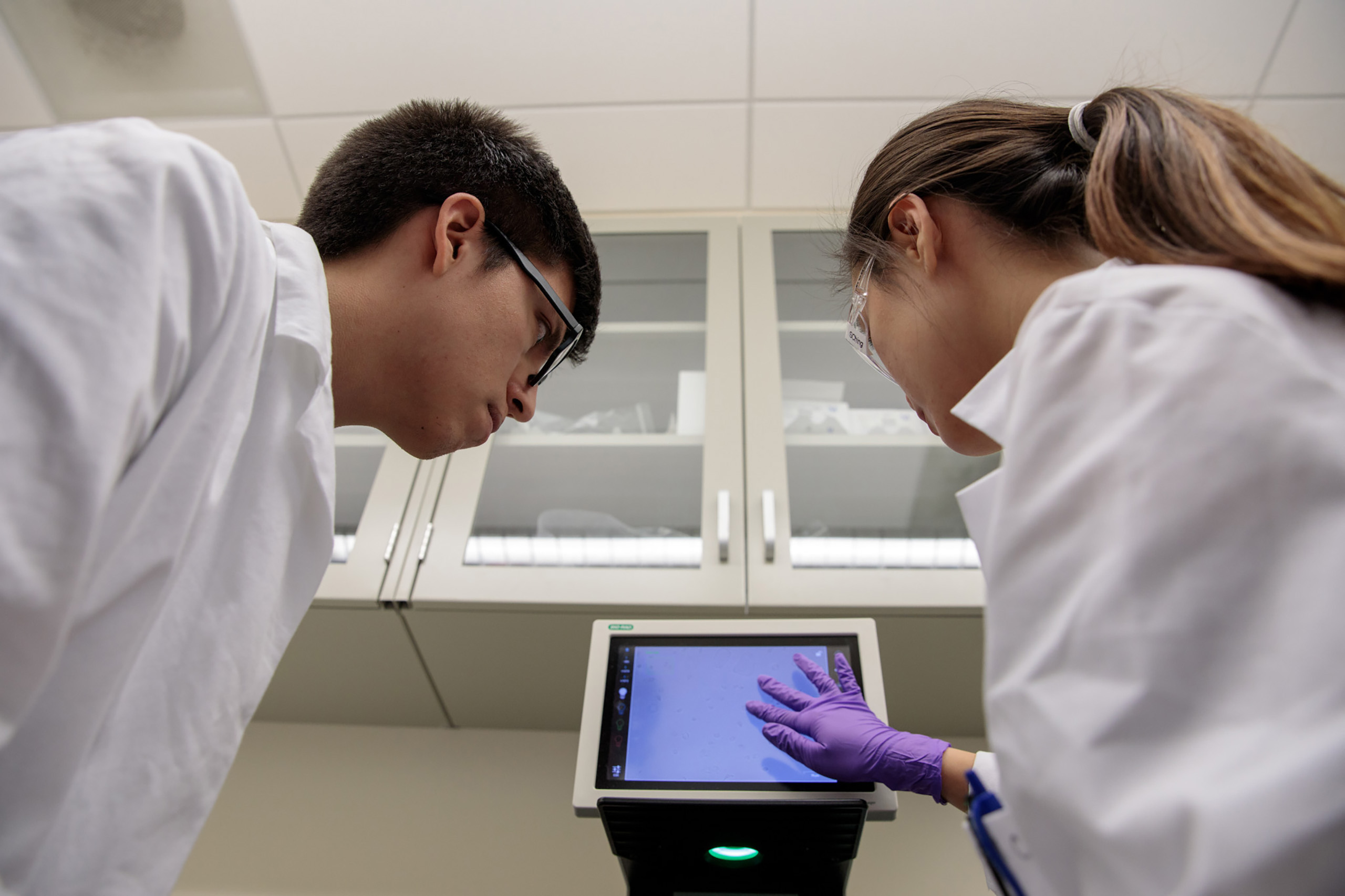 Researcher entering data on a screen in a laboratory while being watched by a student